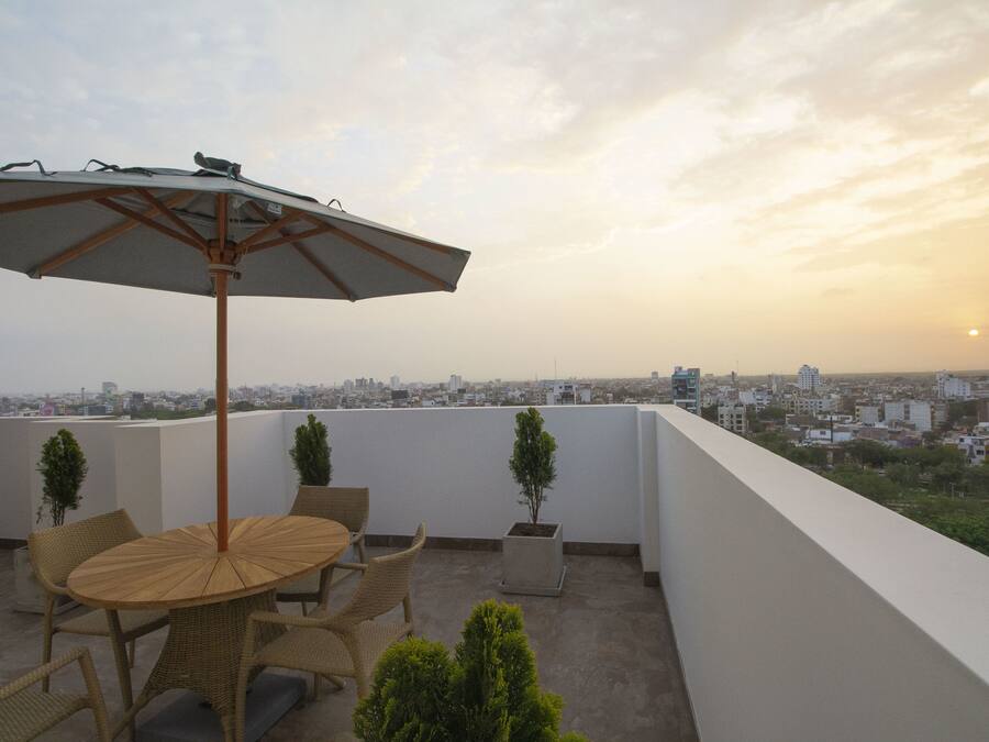 A rooftop terrace with a round table and chairs, a large umbrella, and potted plants.