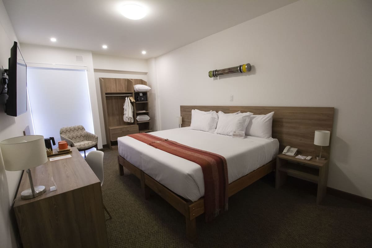 A hotel room with a large bed, a desk with a lamp, a wardrobe, and a TV mounted on the wall.