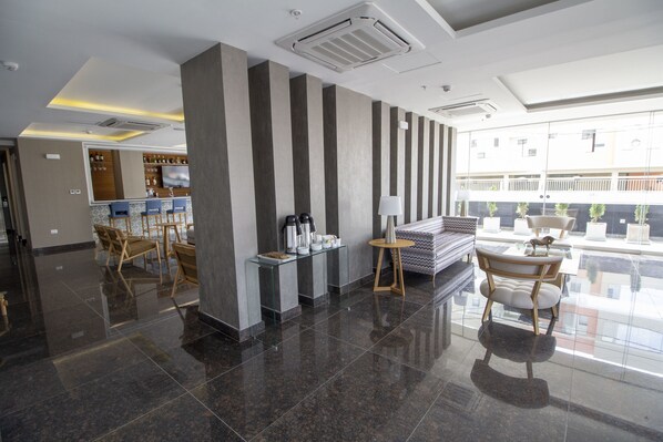 Un vestíbulo moderno con zona de bar, asientos y un amplio ventanal que ofrece vistas del exterior del edificio.