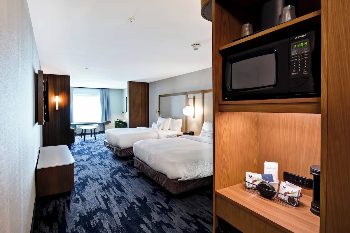 A hotel room with two beds, a desk, a microwave, and a coffee machine.