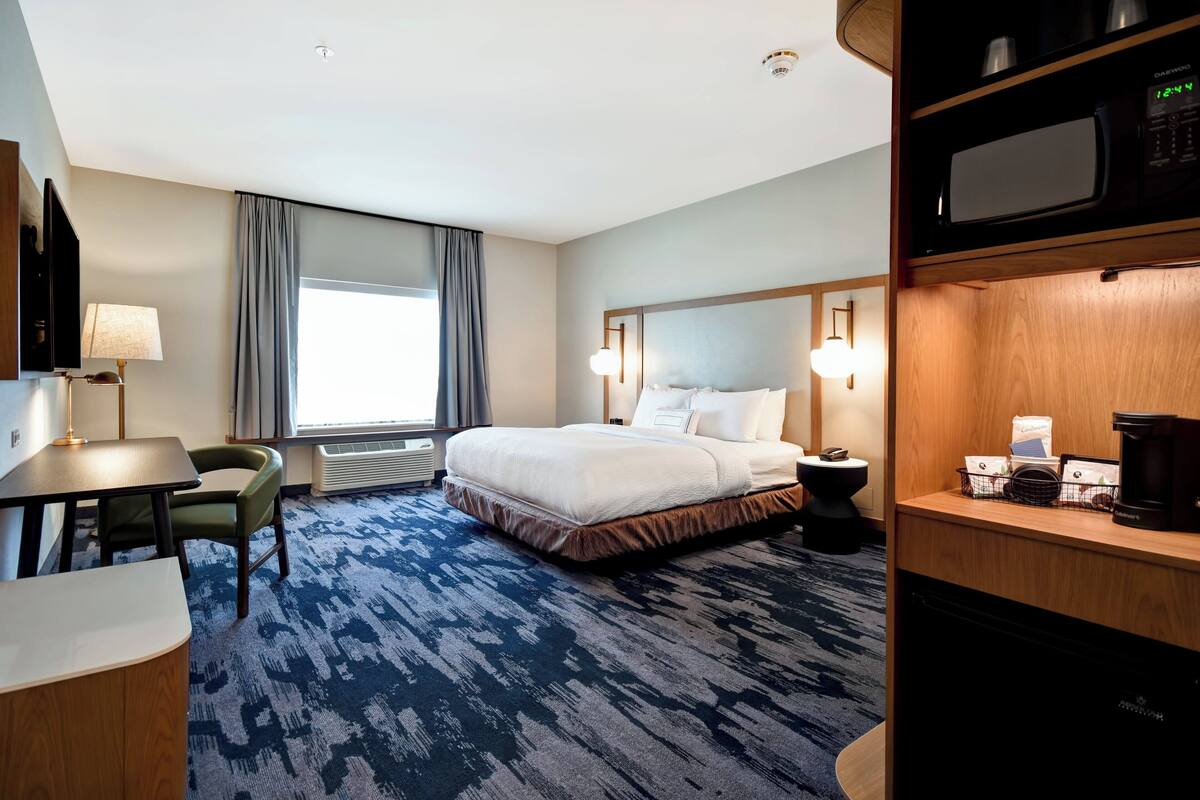 A hotel room with a bed, a desk, a chair, a TV, a microwave, and a coffee machine.