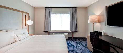 A hotel room with a large bed, a desk, a chair, a TV, and a window with curtains.