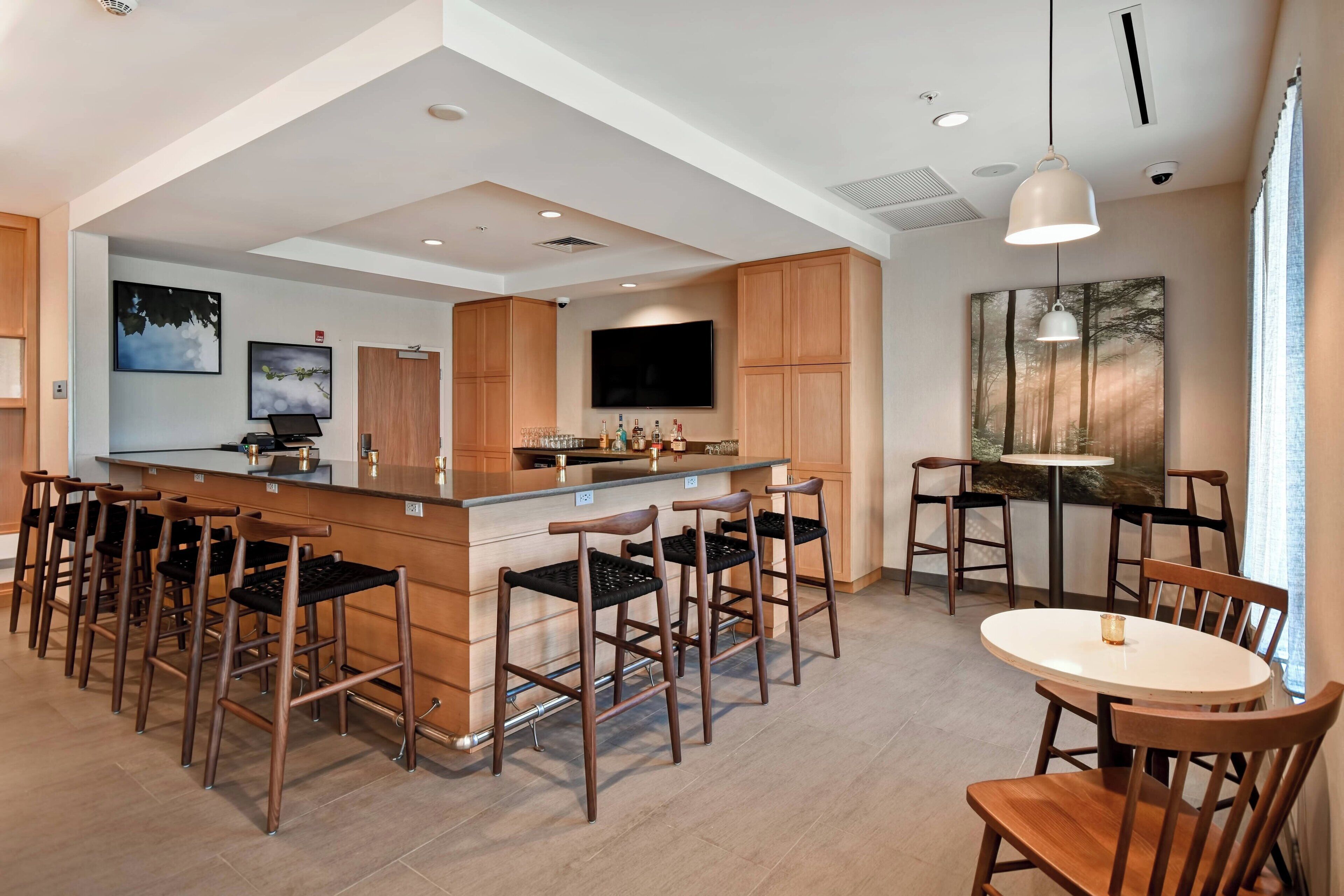 A modern kitchen with a central island, bar stools, a dining table, and a large TV mounted on the wall.
