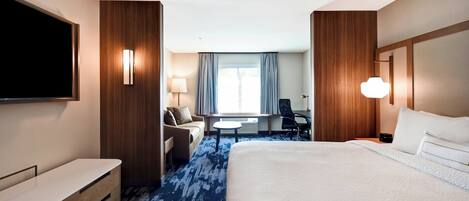 A hotel room with a large bed, a desk, a chair, a TV, and a window with curtains.