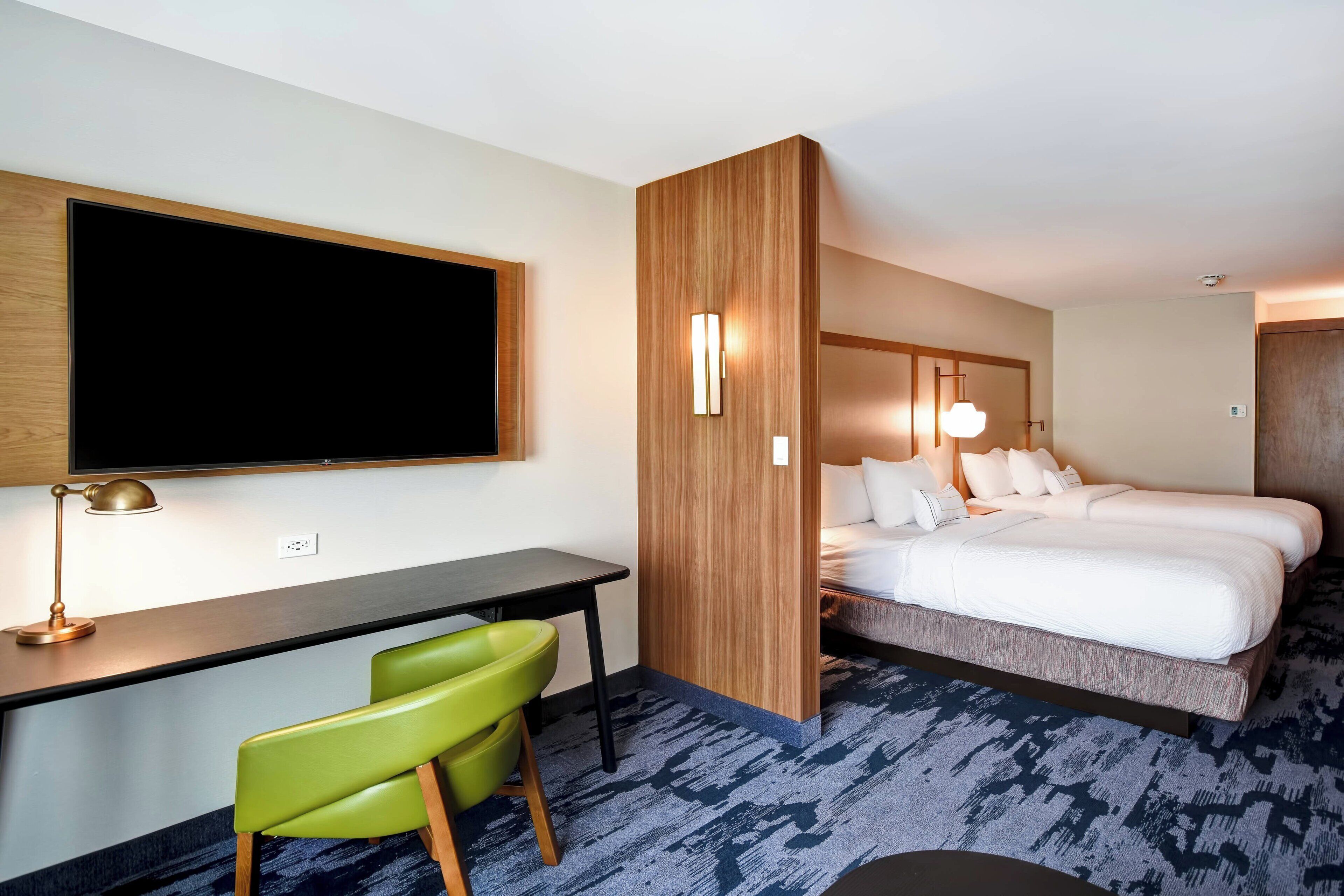 A hotel room with a bed, desk, and green chair.