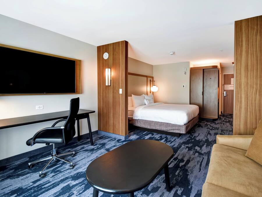 Une chambre d’hôtel comprenant un lit, un bureau avec une chaise, un canapé et un téléviseur à écran plat fixé au mur.