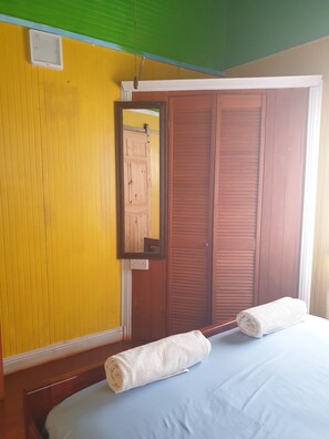 A room with a yellow wall, a wooden door, a mirror, and a bed with two white towels.