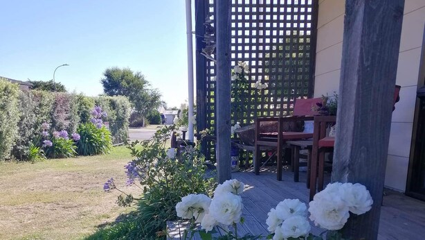 Un giardino con fiori bianchi e viola di fronte a un pontile di legno e un’area porticata.