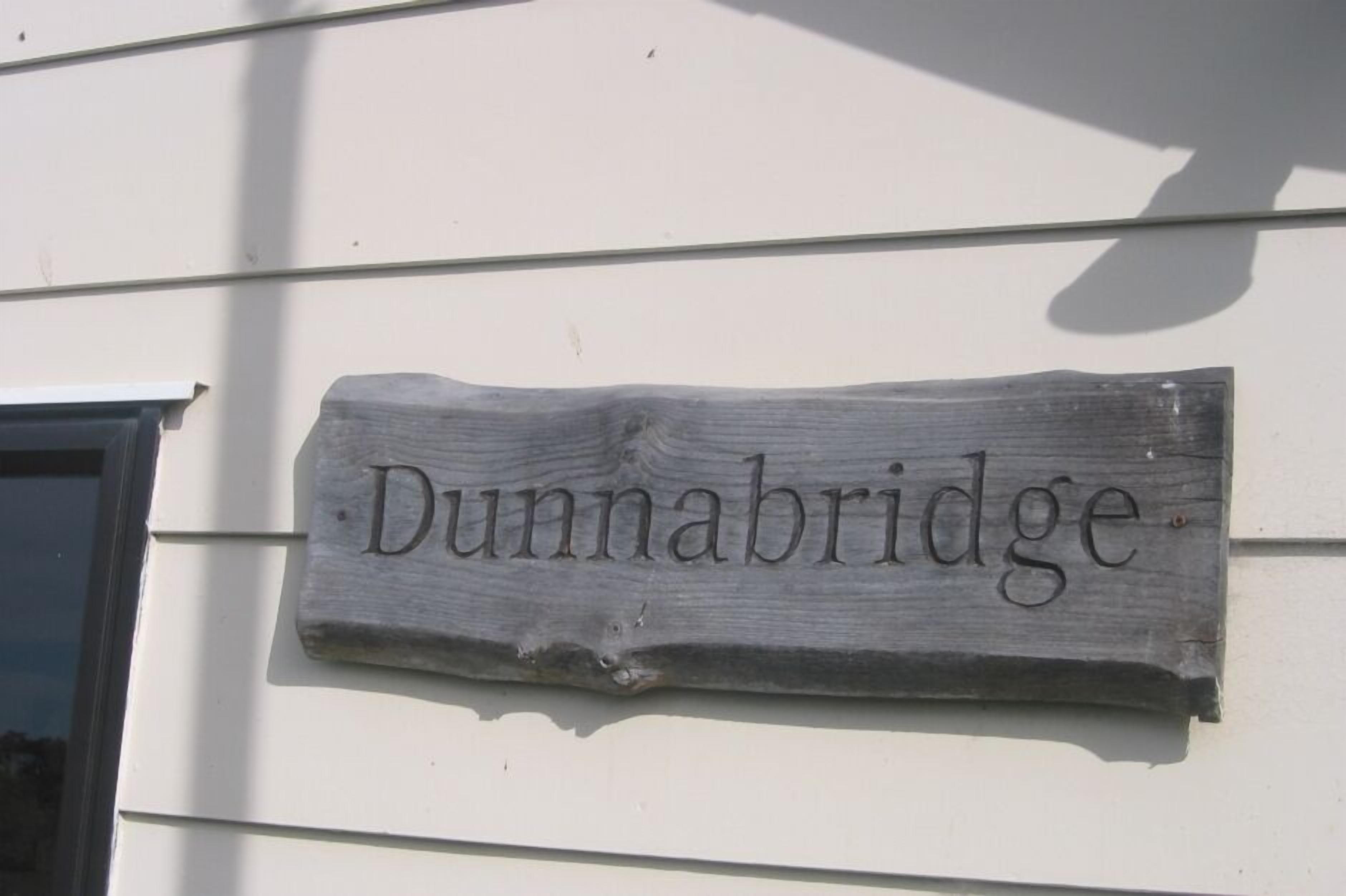 Ein hölzernes Schild mit dem Namen 'Dunnabridge' an einem Gebäude befestigt.