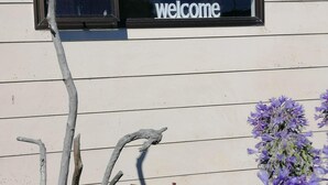 Un edificio con un cartello 'Welcome' sopra una finestra, un vaso blu con bastoncini e fiori viola.