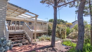 A house with a covered porch, outdoor stairs, and a garden with trees and shrubs.