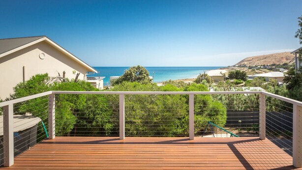 Um deck de madeira com guarda-corpo branco, com vista para a praia e oceano.