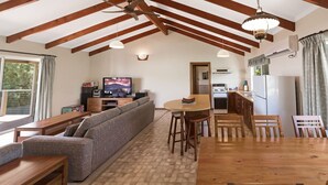 Uma sala de estar aconchegante com sofá, televisão, mesa de jantar de madeira e área de cozinha.