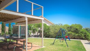 Uma área de pátio com mesas de piquenique, balanço e um espaço coberto para sentar.