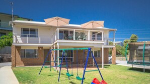 Um edifício residencial de dois andares com varanda, balanço e trampolim no quintal.