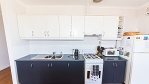 A compact kitchen with white upper cabinets, a black lower cabinet, a gas stove, a microwave, and a refrigerator. - 20 Lady Bay Road Normanville (Normanville)