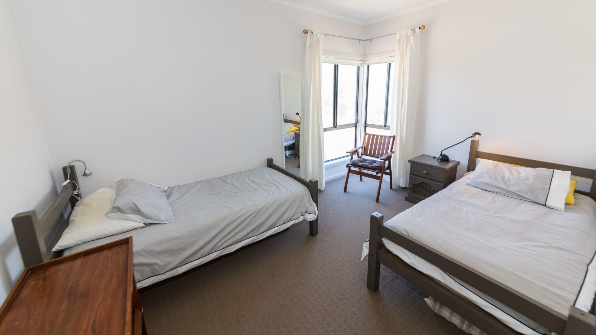 Une chambre avec deux lits simples, une chaise, une table de chevet et une fenêtre avec des rideaux.