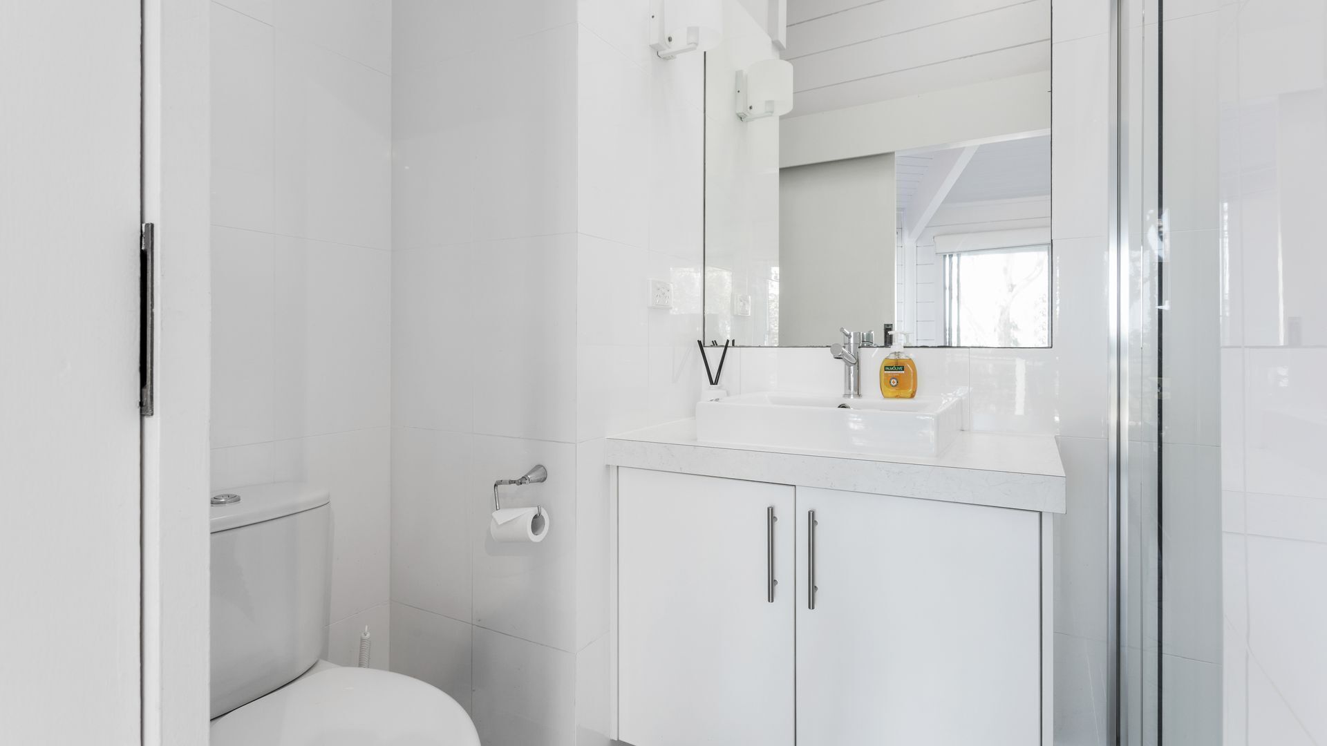 A modern bathroom with a toilet, a sink with a mirror, and a shower area.