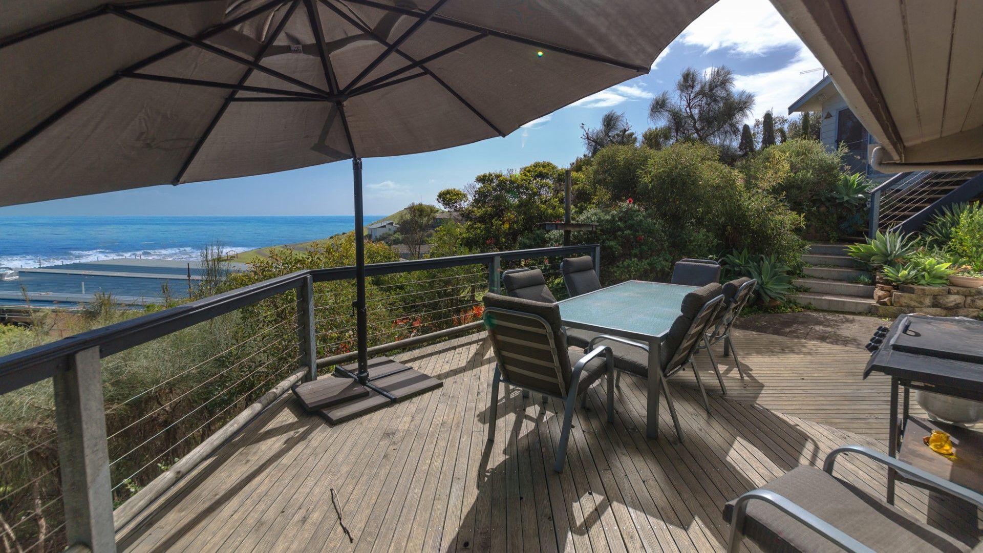 A wooden deck with a table and chairs, overlooking a coastal view.