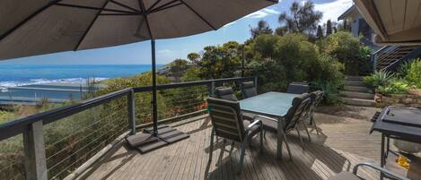 A wooden deck with a table and chairs, overlooking a coastal view.