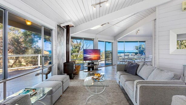Una sala de estar moderna con un televisor grande, asientos cómodos y un balcón con vista al mar.