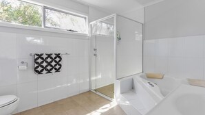 Un baño moderno con cabina de ducha de vidrio, una bañera blanca y un inodoro.