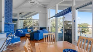 Un espacio habitable amplio con un conjunto de sofá azul, una mesa de comedor de madera y grandes ventanales con vistas al exterior.