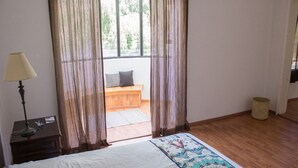 A bedroom with a bed, a bench, a lamp, and a window with curtains.