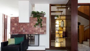 A modern living room with a black sofa, a decorative wall with a plant, and a wooden staircase leading to another room.