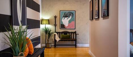 A hallway with a wooden bench, a lamp, and a framed artwork on the wall.