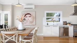 A modern kitchen with white cabinetry, a wooden dining table, and a large window. - Amber Cottage - country cottage (Bowral)