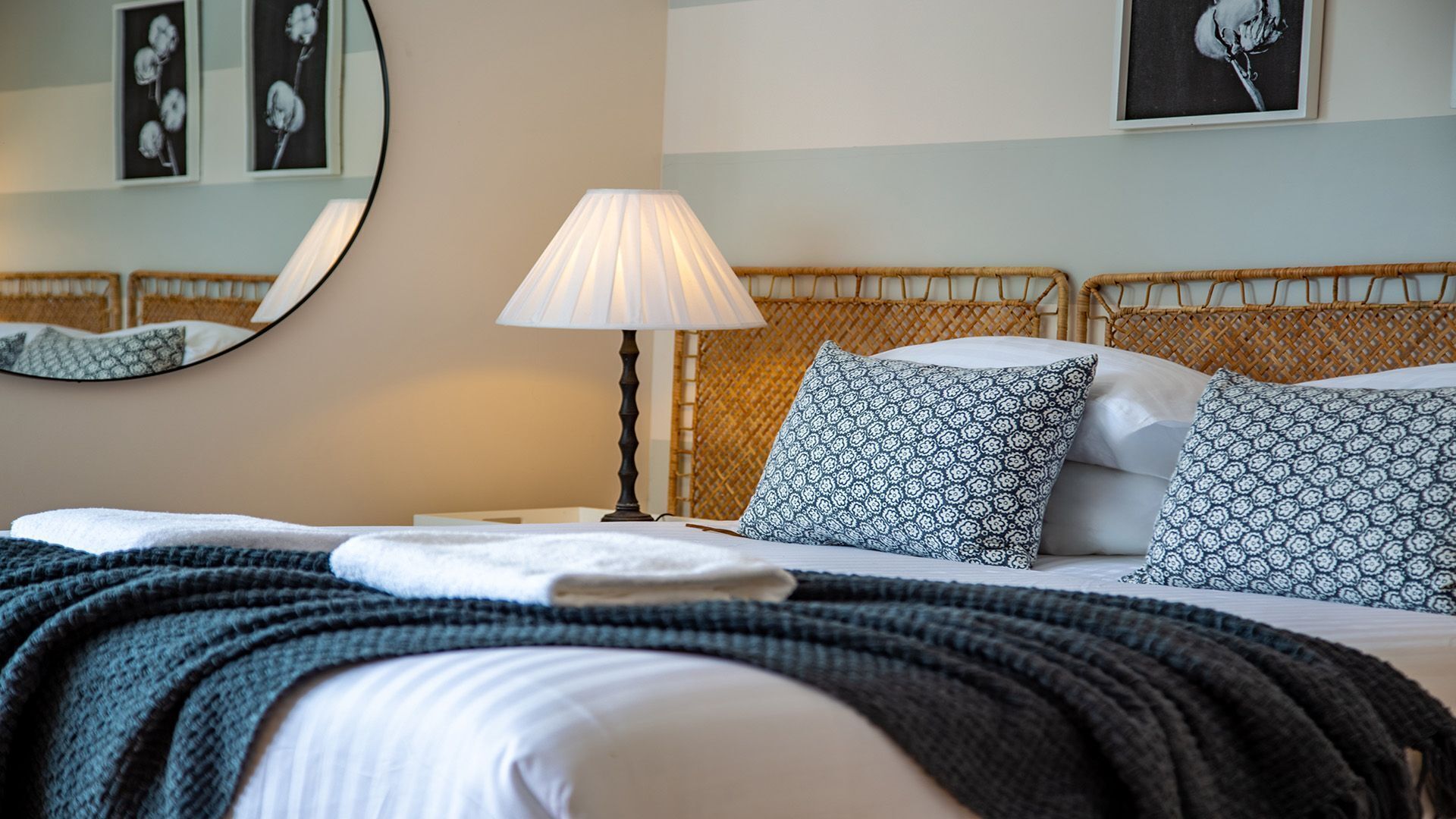 Un lit bien fait, agrémenté d’oreillers à motifs, une lampe de chevet et un miroir au mur.