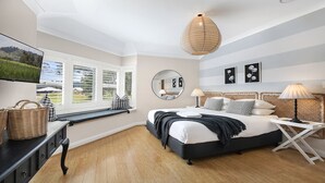 A bedroom with a bed, bedside table, lamp, and a large window with blinds. - Amber Cottage - country cottage (Bowral)