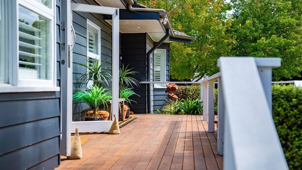 A wooden deck with potted plants, a white railing, and a house with dark siding and white trim. - Amber Cottage - country cottage (Bowral)