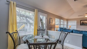 Ein Essbereich mit einem runden Glastisch, vier Stühlen, einem blauen Sofa und einem Fenster mit Jalousien.