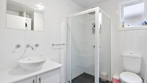 Ein modernes Badezimmer mit einer Duschkabine, einem weißen Waschbecken und einer Toilette.