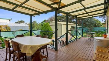 An outdoor covered patio with a table and chairs, surrounded by a wooden deck and a green fence.