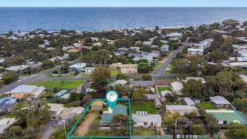 An aerial view of a coastal residential area with houses, roads, and a large body of water in the background.