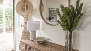 Een houten console tafel met een witte lamp en een vaas met groene bladeren.