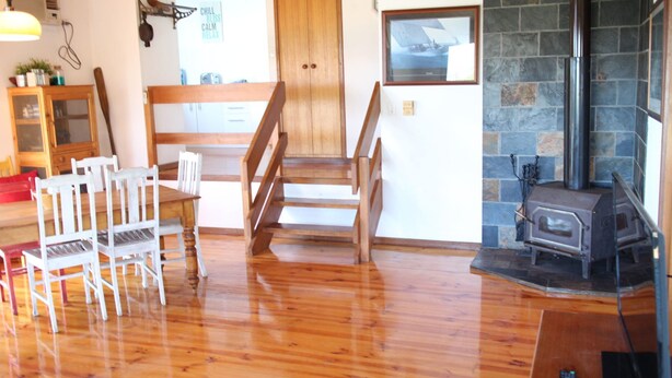 A cozy room with wooden flooring, a dining table with chairs, a wooden bench, a fireplace, and a stone wall. - Tree Top - 4 Robert Norman Street (NORMANVILLE)