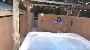 A hot tub under a wooden pergola with string lights, surrounded by walls and a tiled mosaic. - Peaceful Adobe w Jacuzzi, Walk To Arroyo Seco, Pets Welcome (Arroyo Seco)