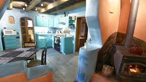A rustic kitchen with teal cabinets, a wood-burning stove, and a dining area with a table and chairs. - Peaceful Adobe w Jacuzzi, Walk To Arroyo Seco, Pets Welcome (Arroyo Seco)