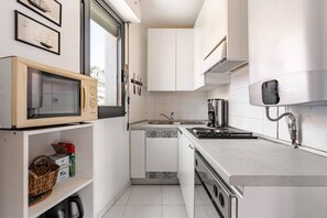 Cuina compacta amb armaris blancs, microones, rentapelats i fogó.