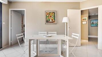 A dining area with a white table and chairs, a painting on the wall, and a door leading to another room.