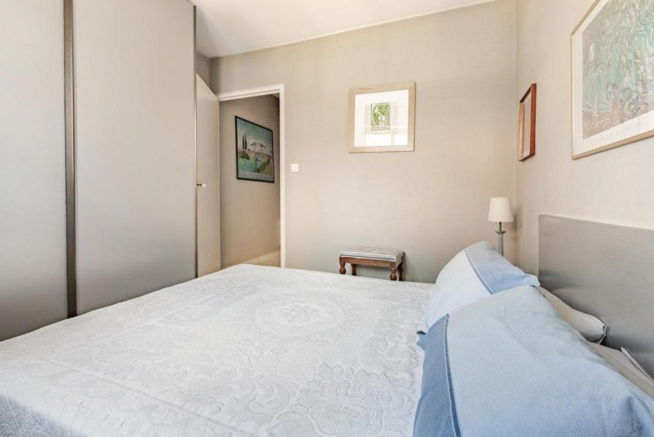 Een slaapkamer met een bed, een nachtkastje, een wandlamp en ingekaderde foto's.