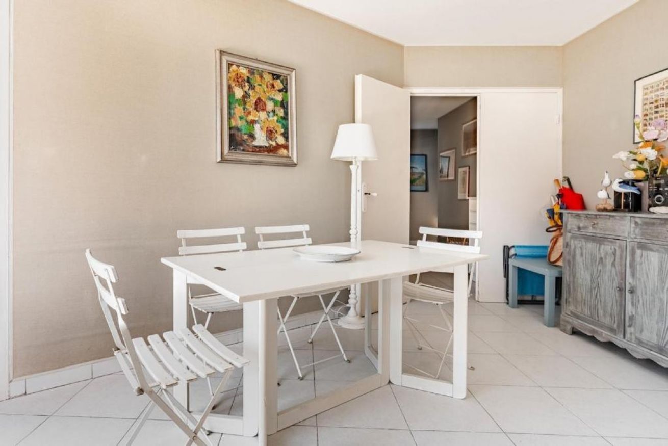 Un coin repas avec une table et des chaises blanches, une lampe et un tableau au mur.