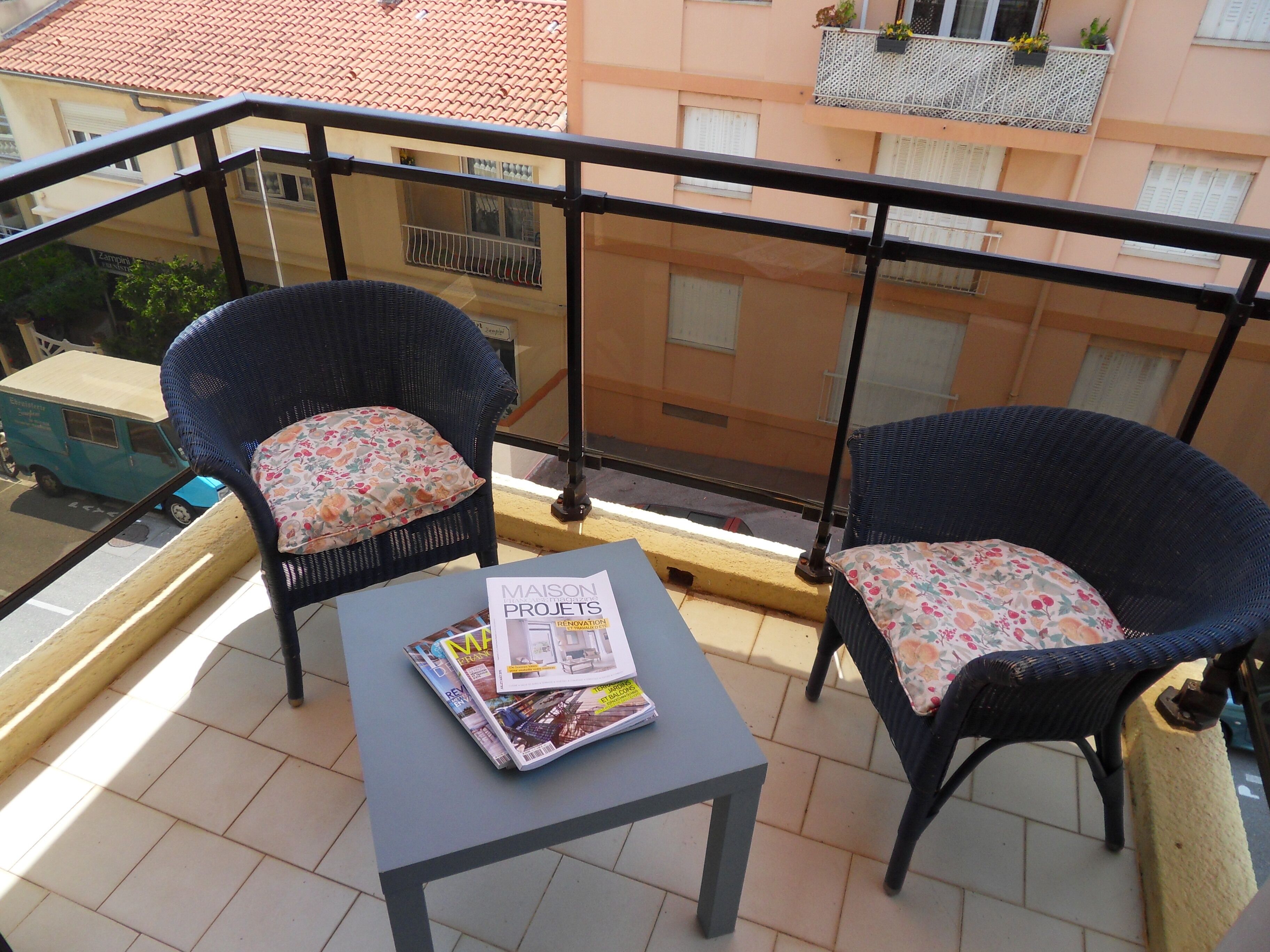 Een balkon met twee rieten stoelen, een tafeltje en een tijdschrift.