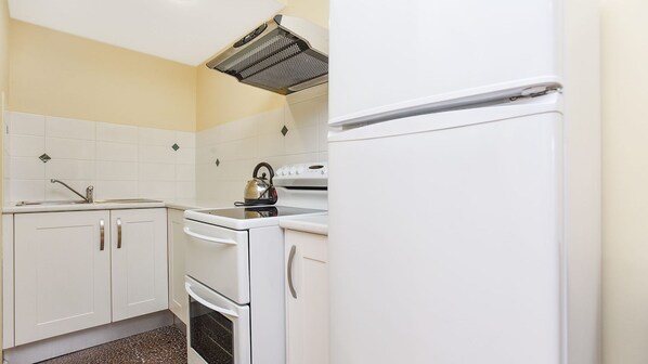 Una cocina compacta con muebles blancos, estufa, horno, hervidor y refrigerador.