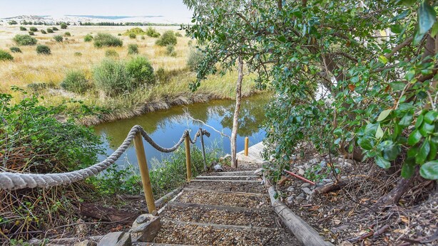 A wooden staircase leading down to a river, surrounded by greenery and a rope barrier. - By the Beach - 30 Jetty Road (Normanville)