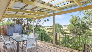 An outdoor patio with a table and chairs, a pergola with a metal roof, and a view of a natural landscape. - By the Beach - 30 Jetty Road (Normanville)